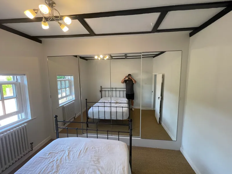 Full-wall mirrored sliding wardrobe in a beamed period bedroom.