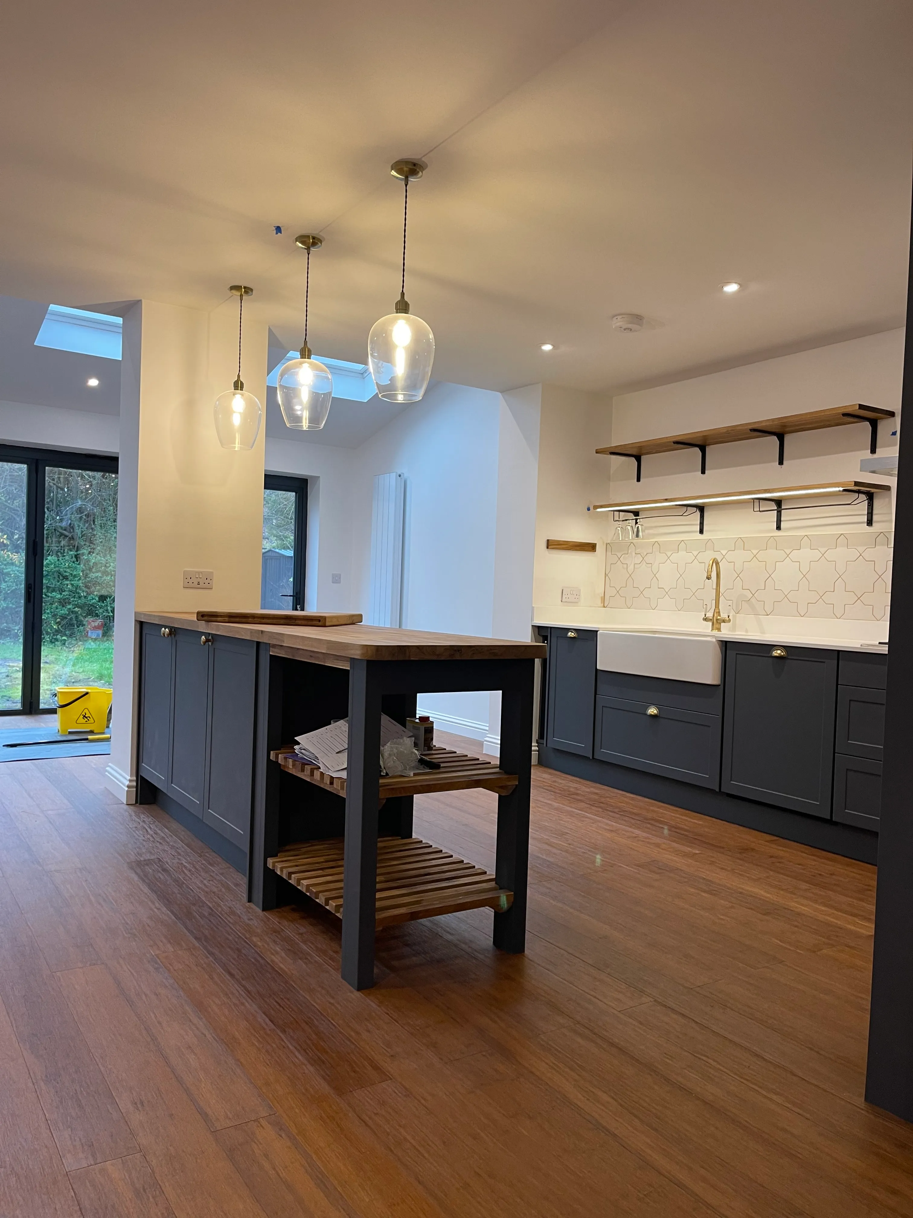 Navy shaker kitchen with oak open shelving, plate rack, and garden door.