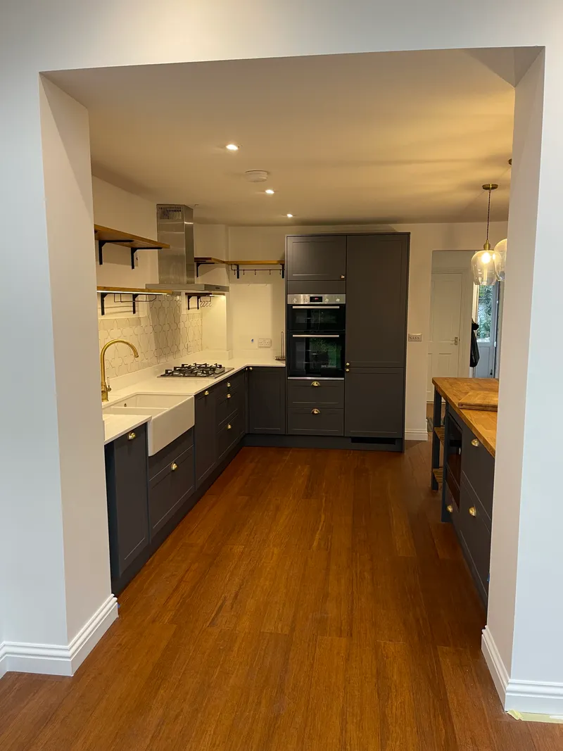 Wide view of a navy and white shaker kitchen with oak parquet floor, range cooker, and butler sink.
