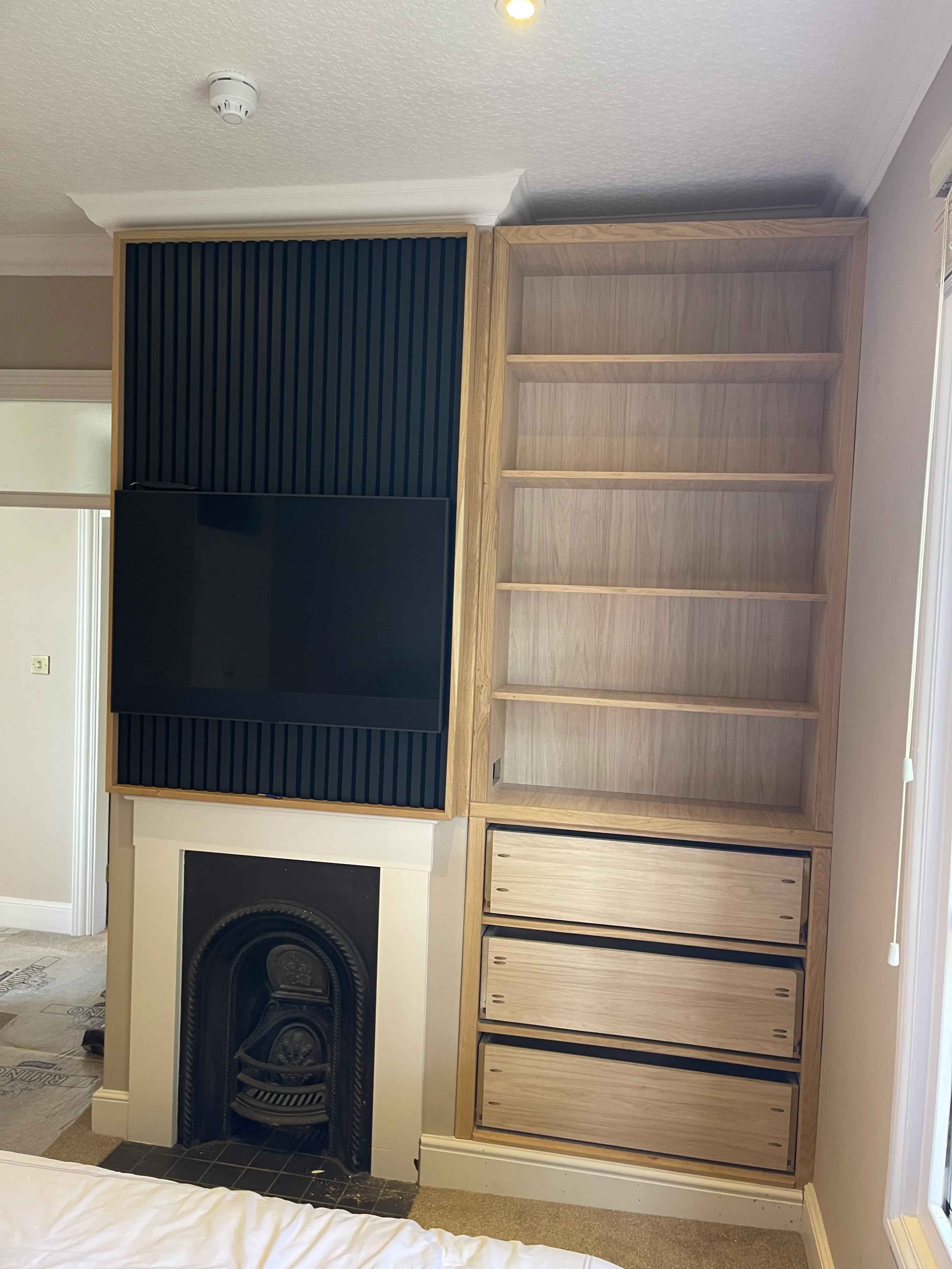 Bespoke oak media wall with a fluted TV panel above a cast-iron fireplace.