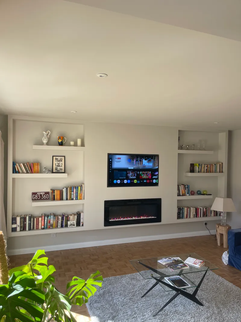 White recessed bookcase media wall with central TV and styled book and vinyl display.