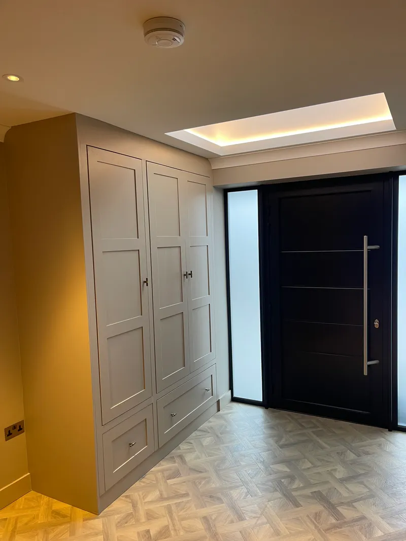 Painted shaker hallway storage cabinet under a coffered skylight with parquet flooring and dark front door.